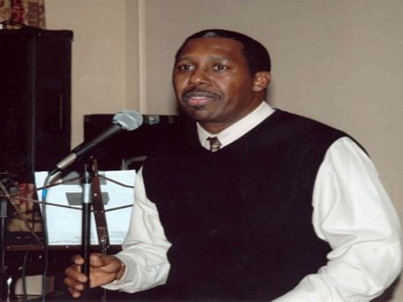 Larry B. Scott while holding a mike wearing a black and white shirt inside a room