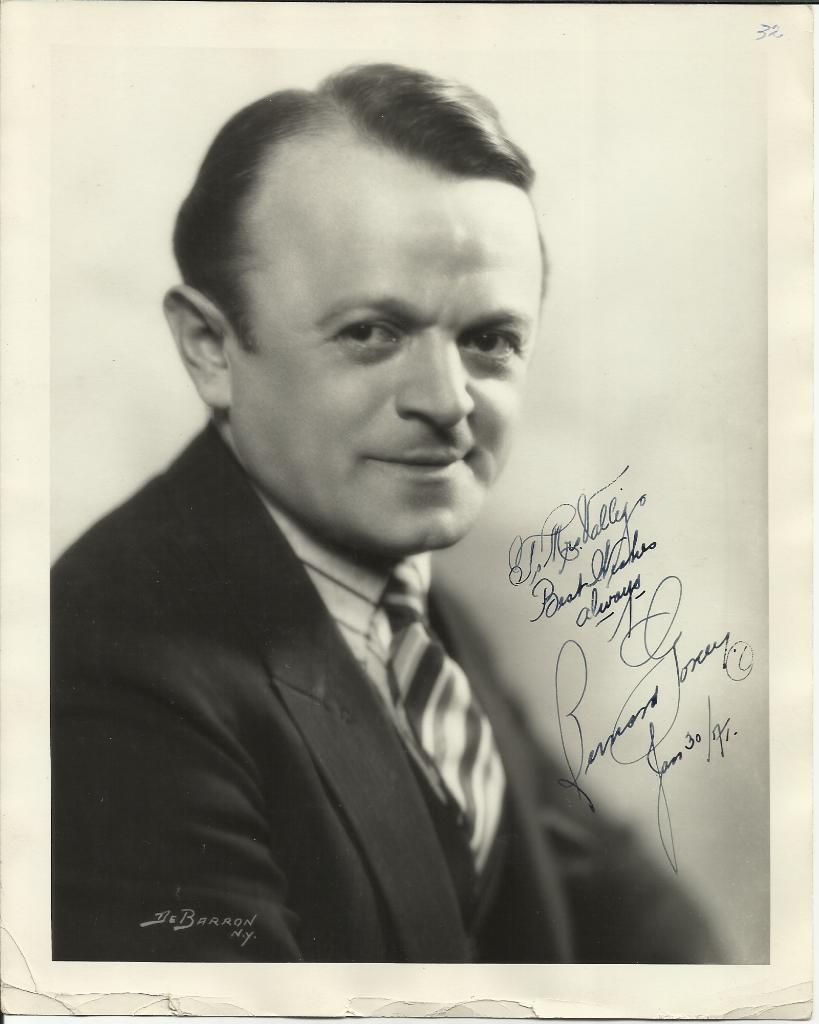 On the left, Leo Gorcey with a tight-lipped smile, wearing a black coat over white long sleeves, and a striped necktie. On the right, is an autograph of Leo Gorcey.